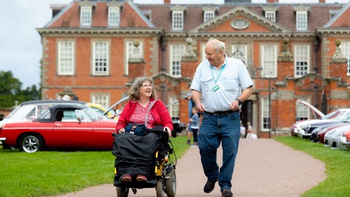 A visitor and companion using a mobility scooter on the path leading up to Hanbury Hall